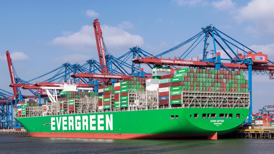 Stort grönt Evergreen containerfartyg lastat med färgglada fraktcontainrar, dockat vid en livlig hamnterminal.