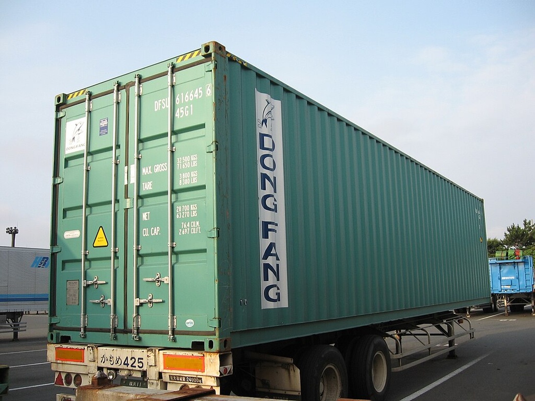En stor grön fraktcontainer med 'DONG FANG'-märkning monterad på en lastbilstrailer i en hamnanläggning.